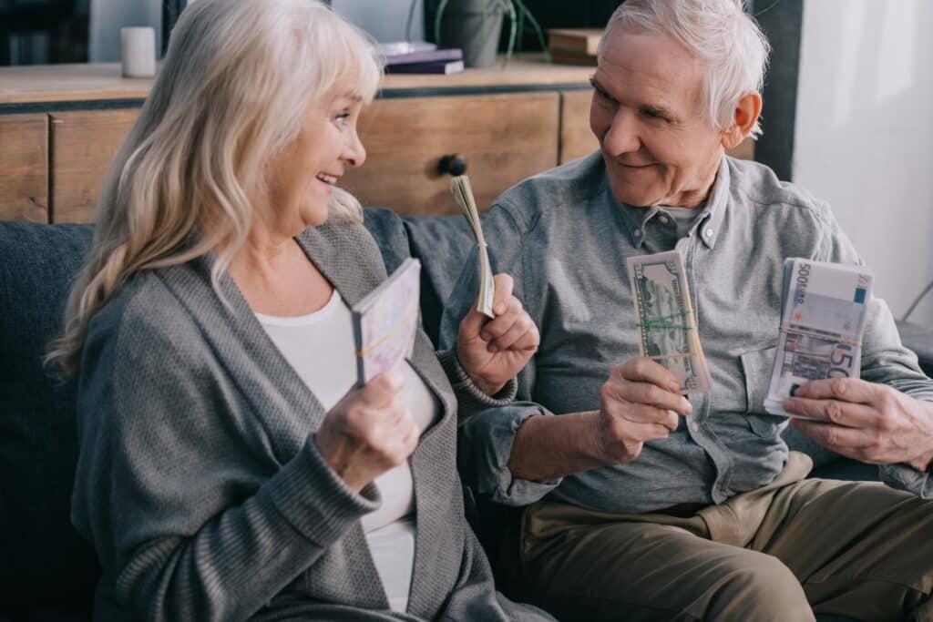 happy senior couple sitting on couch and holding euro and dollar banknotes